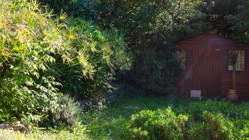 A wooden shed in a garden with dense foliage and a stone wall in the background.