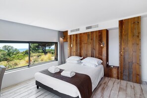 A modern bedroom with a large bed, a view of the outdoors, and wooden paneling on the walls.