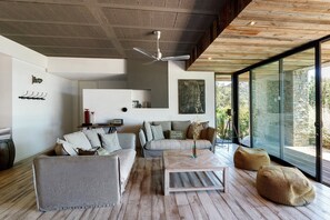 A modern living room with a ceiling fan, a sofa set, a coffee table, and a large window with a view.