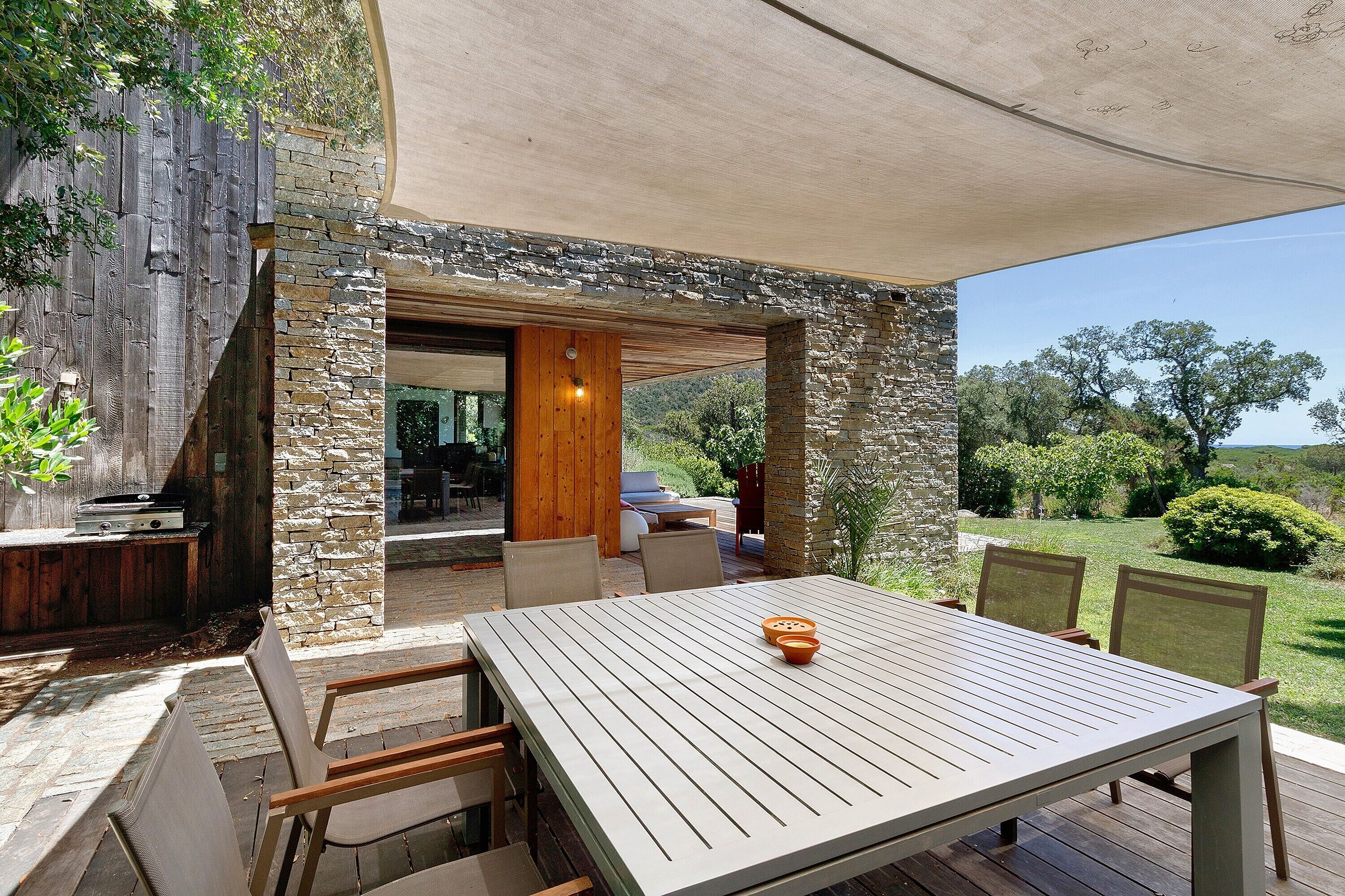 Um pátio externo com mesa e cadeiras, uma parede de pedra e vista para a paisagem ao redor.