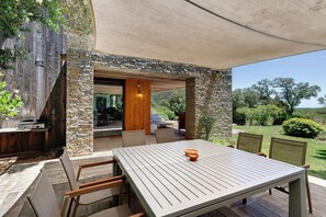 Une terrasse extérieure avec une table et des chaises, un mur en pierre et une vue sur le paysage environnant.