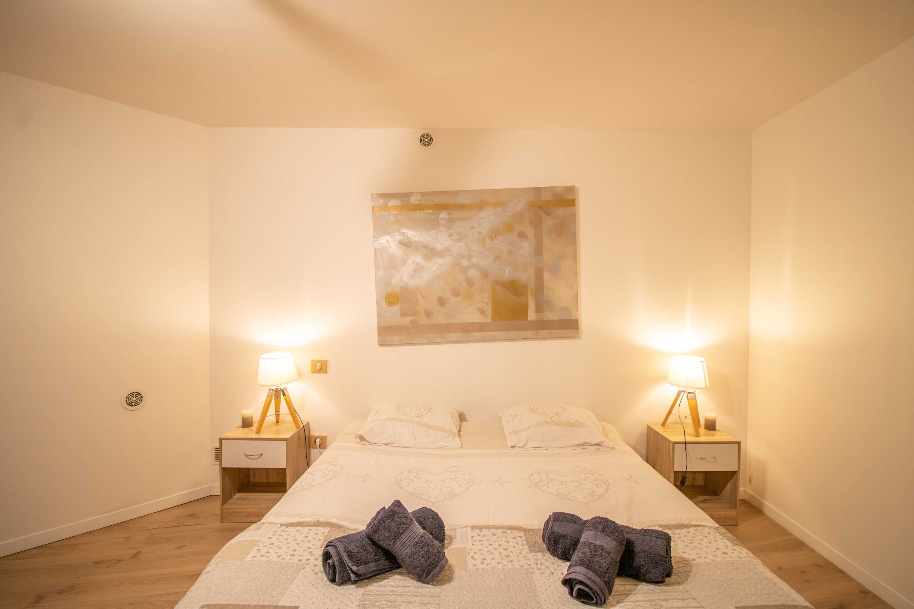 Een hotelkamer met een bed, twee bedlampen, een nachtkastje met een lade, en een aan de muur hangend schilderij.