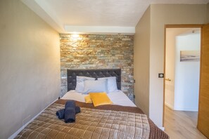Une chambre avec un mur en pierre, un lit doté d’une tête de lit capitonnée, une porte en bois et un tableau accroché au mur.