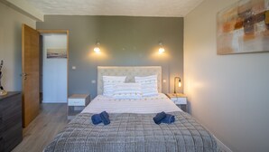 Ein Schlafzimmer mit Bett, Nachttischen, einer Tür und einem Bild an der Wand.