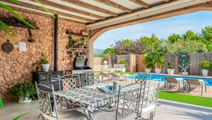 An outdoor patio with a stone wall, a grill, a pool, and lounge chairs.