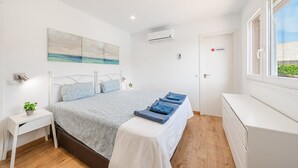 A bedroom with a bed, bedside table, nightstand, and a window.