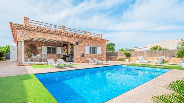 A swimming pool with a stone house, outdoor furniture, and a well-maintained lawn.