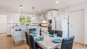 A modern kitchen with white cabinets, a dining table set with blue plates, and a refrigerator.