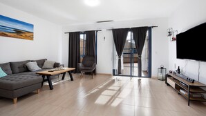 A modern living room with a sectional sofa, a wooden coffee table, a grey armchair, and a TV stand with a flat-screen TV. - Casa Otoño – Holiday Home with Sea View, Private Terrace, and Wi-Fi (La Lajita)