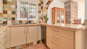 A kitchen with a tiled backsplash, wooden cabinets, a dishwasher, and a window with a view of trees. - Holiday Home 'Tower House' with Sea View, Wi-Fi and Air Conditioning (Competa)