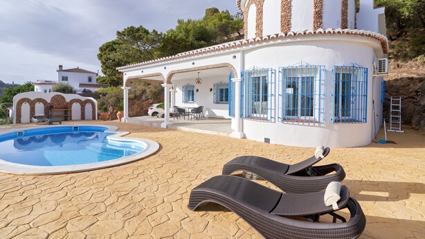 A pool area with lounge chairs, a covered patio, and a white building with blue gates. - Holiday Home 'Tower House' with Sea View, Wi-Fi and Air Conditioning (Competa)