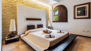 Ein Schlafzimmer mit Steinsturz, einem Bett mit Kopfteil, einem Nachttisch mit Lampe und einem Fenster mit Blick.