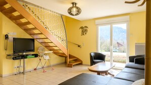 Una sala de estar con un sofá, televisión, una escalera y vistas al exterior.
