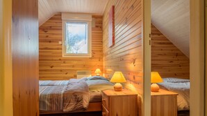 Un dormitorio de cabaña acogedor con paredes de madera, techo inclinado, una ventana y dos mesitas de noche con lámparas.