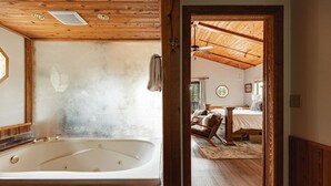 A room with a large bathtub, wooden ceiling, and a bed with a wooden headboard.