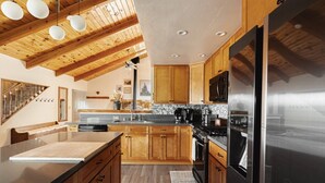 A modern kitchen with wooden cabinets, a stainless steel refrigerator, and a wooden ceiling.