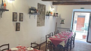 Comedor con mesas dispuestas para una comida, vigas de madera en el techo y botellas de vino en estantes.