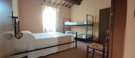 Quarto de dormitório com beliches, uma cama de solteiro, uma cadeira e uma janela com cortinas.