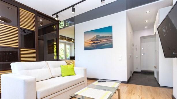 Moderni olohuone, jossa on valkoinen sohva, lasinen sohvapöytä ja maalaus, jossa on kuvattuna vuori.