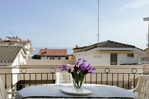 Un balcón con una mesa, un jarrón de flores moradas y vistas a edificios vecinos.