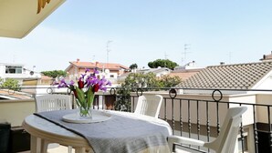 A balcony with a table, chairs, and a vase of flowers.