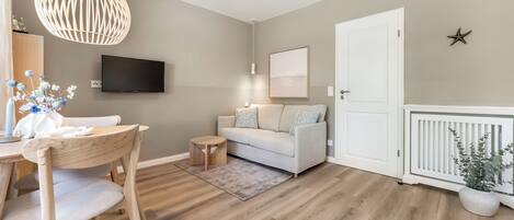 A modern living room with a sofa, a dining table with chairs, a TV mounted on the wall, and a decorative star on the wall.
