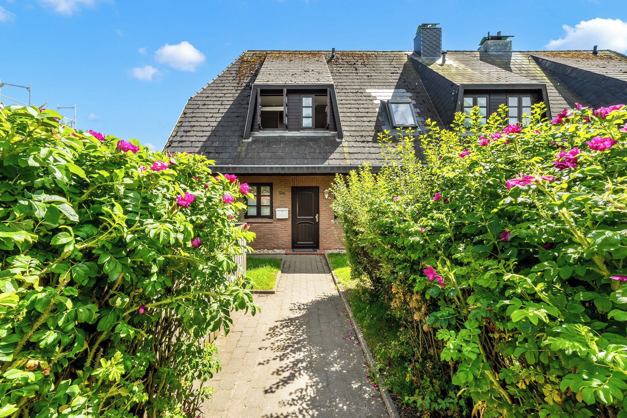 A house with a sloped roof, a front door, and a pathway leading to the entrance.