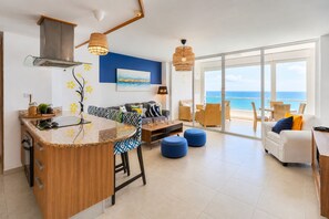 A modern kitchen with a bar area, a dining set, and a living area with a view of the sea.