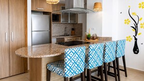 A modern kitchen with a granite countertop, stainless steel appliances, and a bar area with patterned stools.