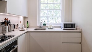 A modern kitchen with white cabinets, a stainless steel sink, a microwave, and a window with a view of trees.
