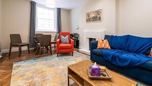 A living room with a blue sofa, a red armchair, a wooden coffee table, and a dining area with chairs and a table.