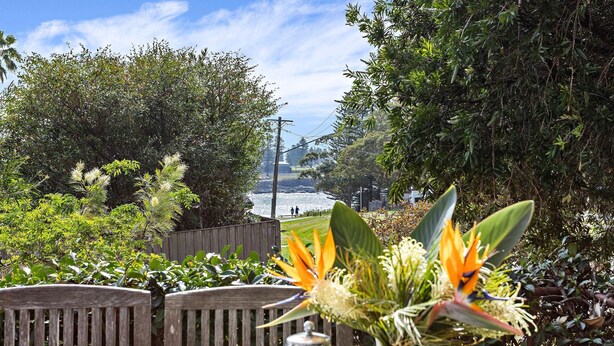 Un jardin avec une clôture en bois, des plantes tropicales et une vue sur un plan d’eau.