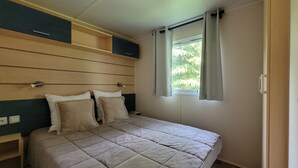 A bedroom with a bed, a window with curtains, and a headboard with storage compartments. - Mobilhome Nicolette, 15 Minutes de Europa-park! (Boofzheim)