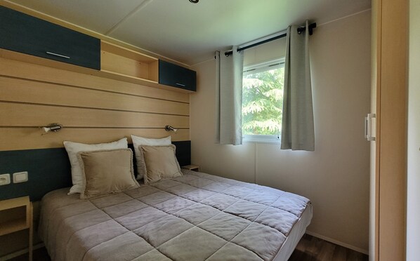 A bedroom with a bed, a window with curtains, and a headboard with storage compartments. - Mobilhome Nicolette, 15 Minutes de Europa-park! (Boofzheim)
