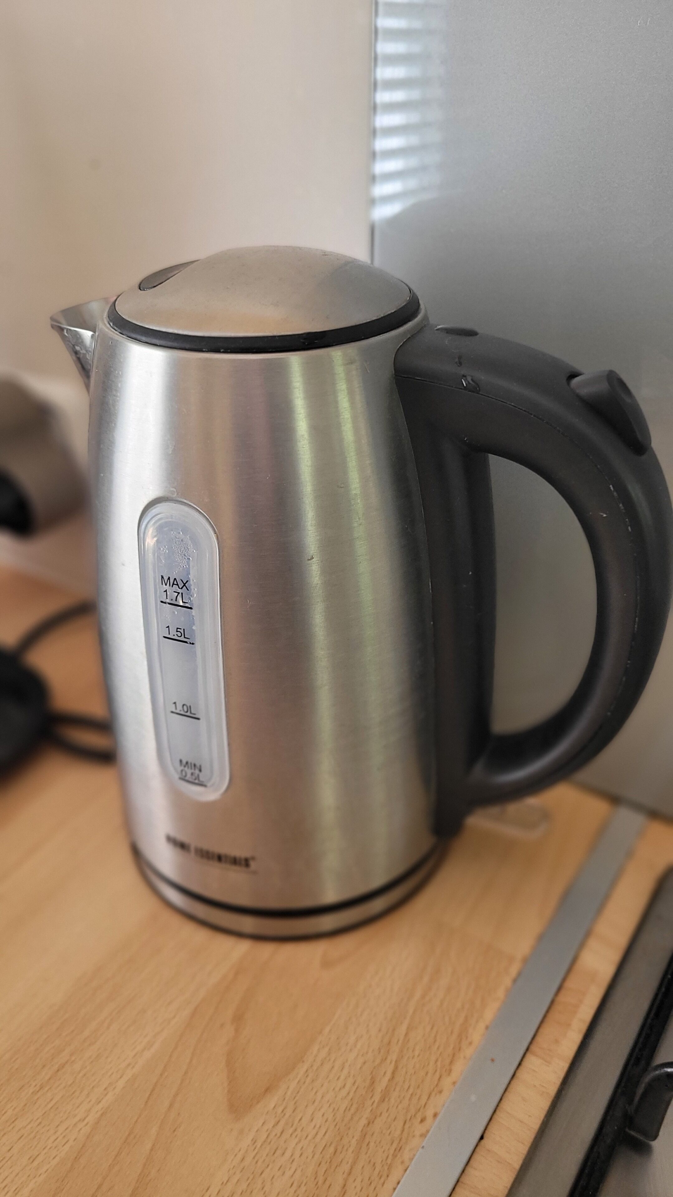 A stainless steel electric kettle with measurement markings on the side, placed on a wooden surface.