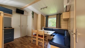 A compact room with a wooden table, chairs, a sofa, a TV, and a window with curtains. - Mobilhome Nicolette, 15 Minutes de Europa-park! (Boofzheim)