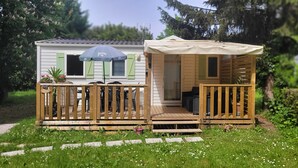 A small wooden house with a balcony, a covered porch, and a garden area with potted plants. - Mobilhome Nicolette, 15 Minutes de Europa-park! (Boofzheim)