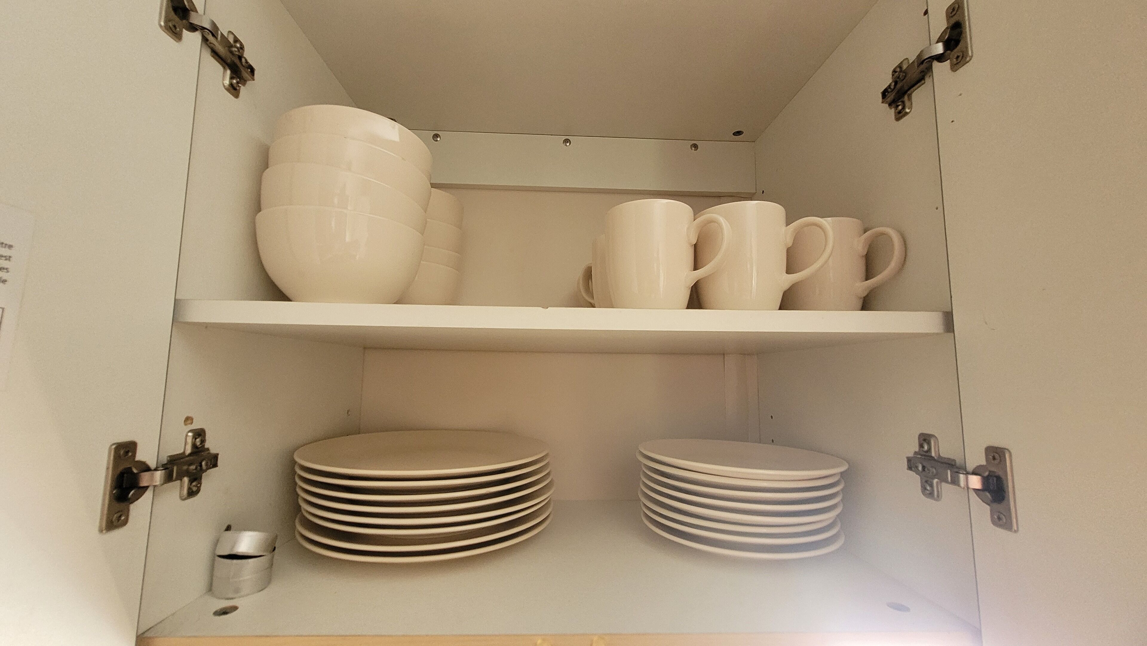 A storage cabinet with shelves holding white plates, bowls, and mugs.