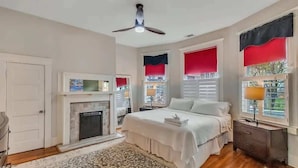 A bedroom with a bed, a fireplace, a nightstand, and a window with red curtains.
