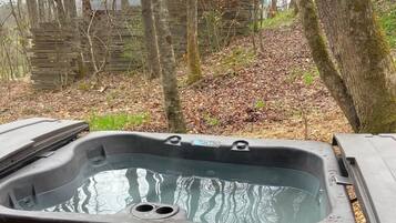 Een hottub op een houten terras, met een bos op de achtergrond.