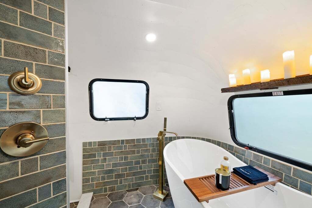 Un baño con una bañera blanca, un ventanal con vistas y una lámpara de pared.
