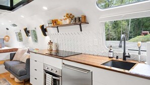 Een moderne keuken met een houten aanrecht, roestvrijstalen apparatuur en een raam met uitzicht op een bos.