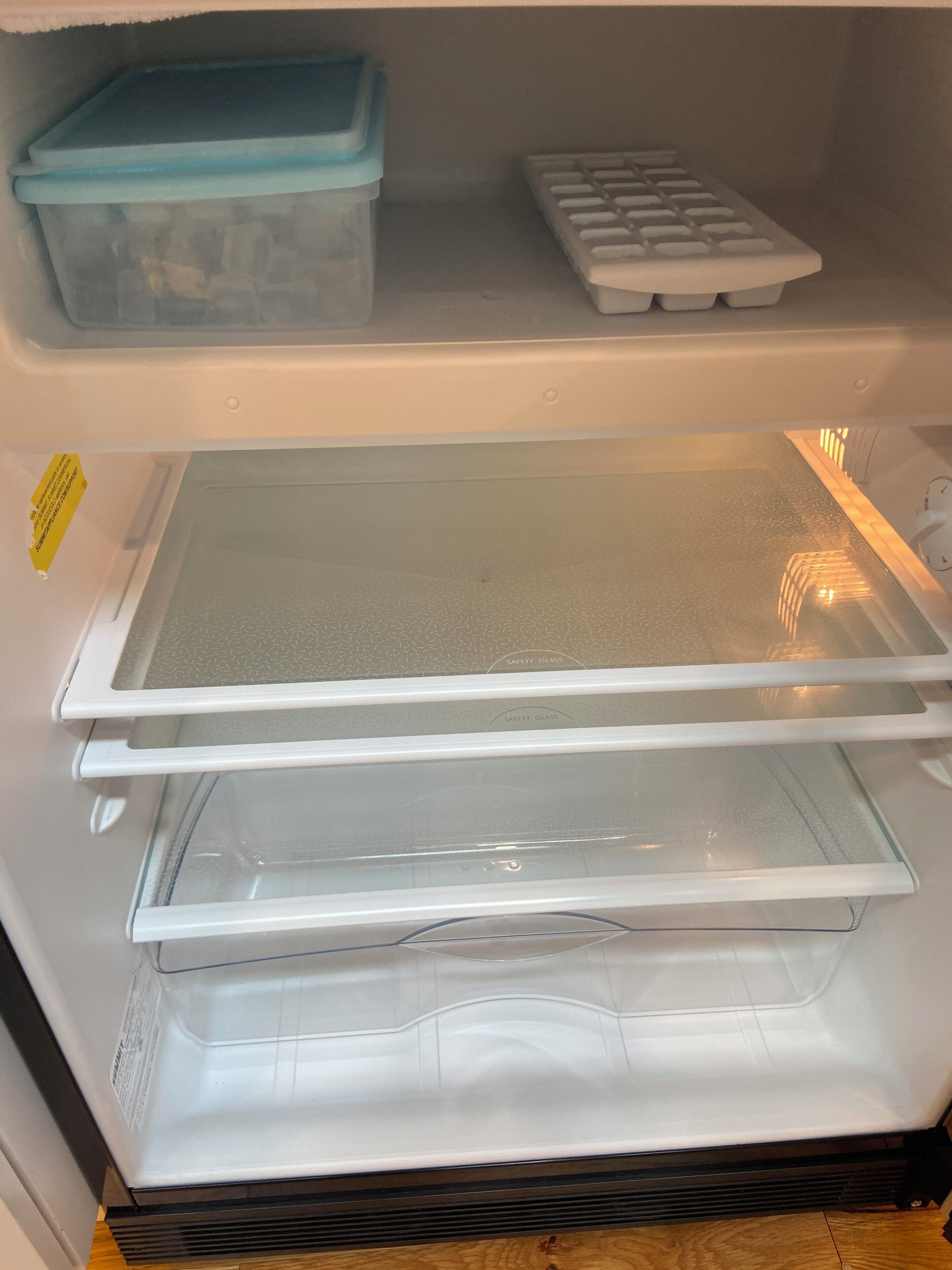 A refrigerator with a clear shelf, a blue storage bin, and a tray of ice cubes.