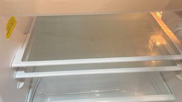 A refrigerator with a clear shelf, a blue storage bin, and a tray of ice cubes.