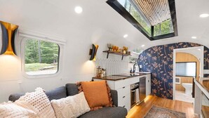 Een ruimtelijk ingerichte leefruimte met een bank, een kitchenette en een raam met uitzicht op groen.