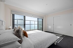 A bedroom with a large bed, a sliding glass door to a balcony, and a white wardrobe.