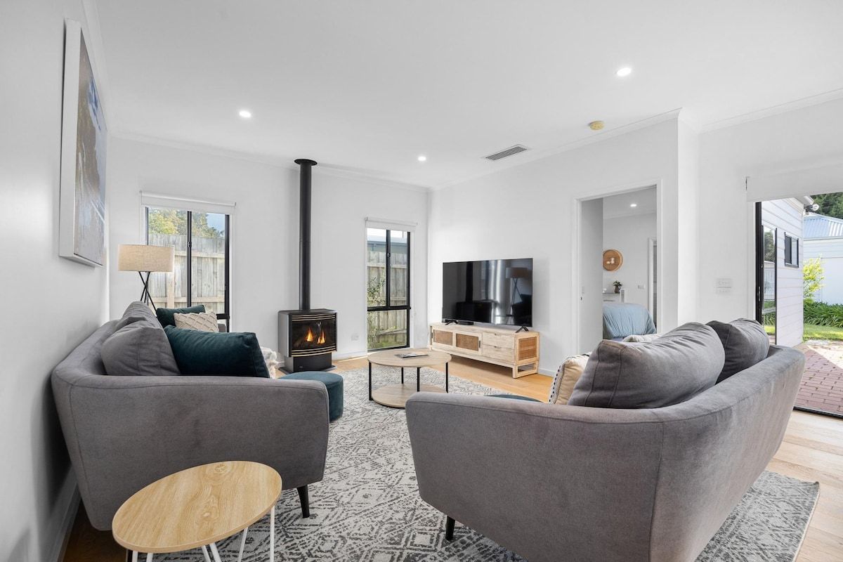 A modern living room with a fireplace, grey sofas, a TV, and a wooden coffee table.