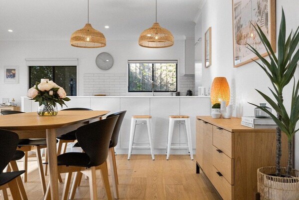 A modern kitchen with a central island, pendant lights, and a dining area with chairs and a table.