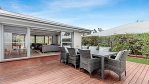 Una moderna terrazza esterna con tavolo e sedie, una porta scorrevole in vetro che dà su una cucina e un pontile in legno.