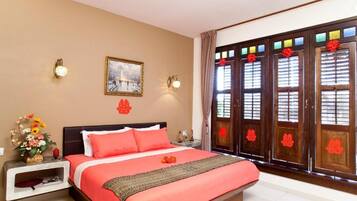 Una habitación de hotel con cama, mesita de noche, lámpara de pared, un cuadro enmarcado y una ventana con detalles decorativos.